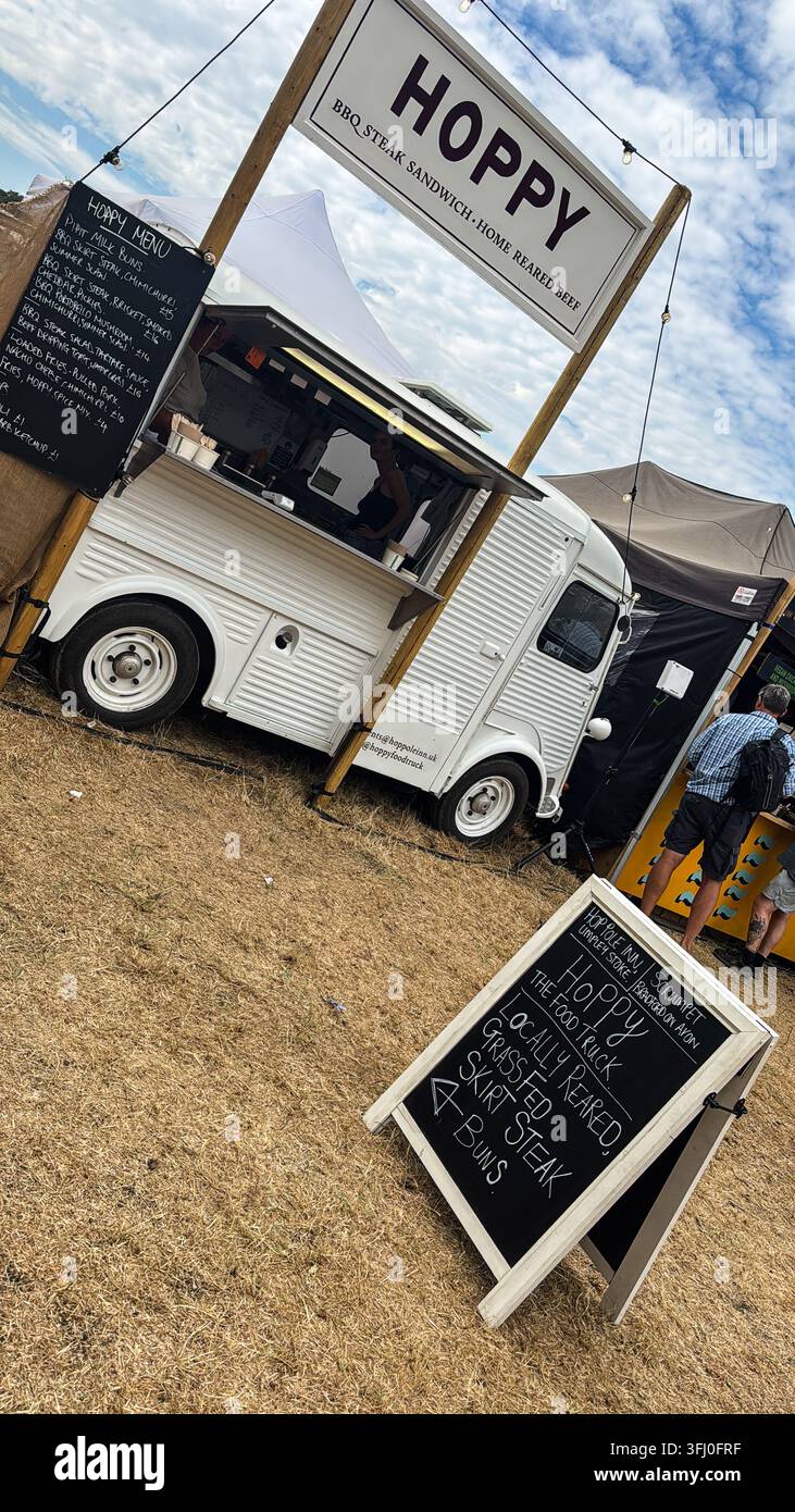 Camion de restauration « Hoppy » servant des sandwichs au steak barbecue et de la bière brassée maison à un festival gastronomique en plein air, avec des menus sur tableau noir et des visiteurs du festival - Image de stock capturée avec un smartphone