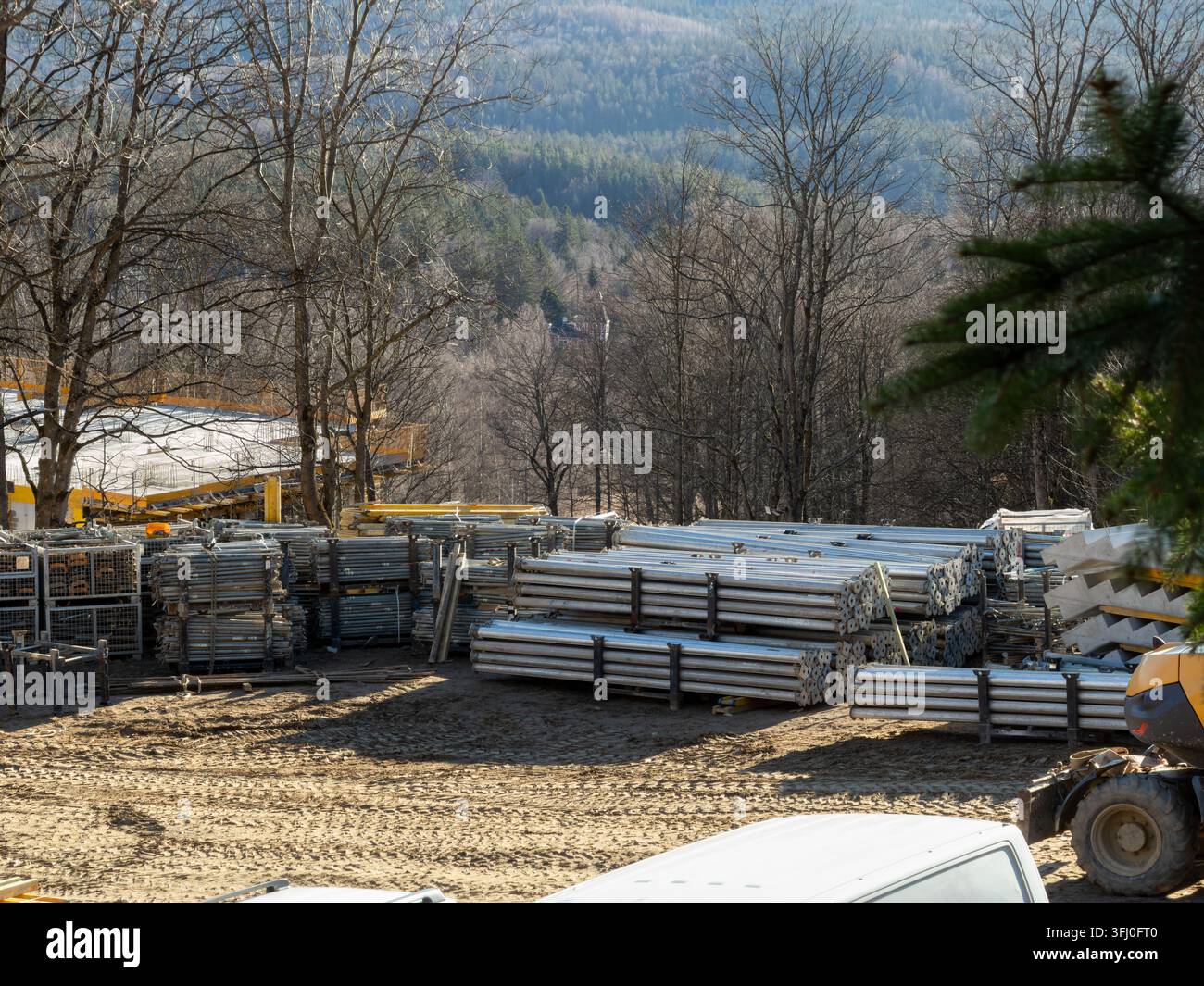 Poutres de construction métalliques organisées sur un terrain en terre près d'un projet de construction entouré de collines boisées, représentant des travaux d'infrastructure lourds et Lan Banque D'Images