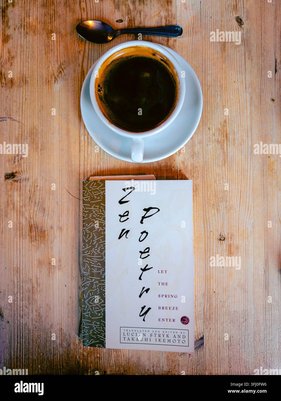Vue aérienne d'une tasse de café noir et d'une cuillère à côté de « Zen Poetry », un livre édité par Lucien Stryk et Takashi Ikemoto, sur une table en bois Banque D'Images