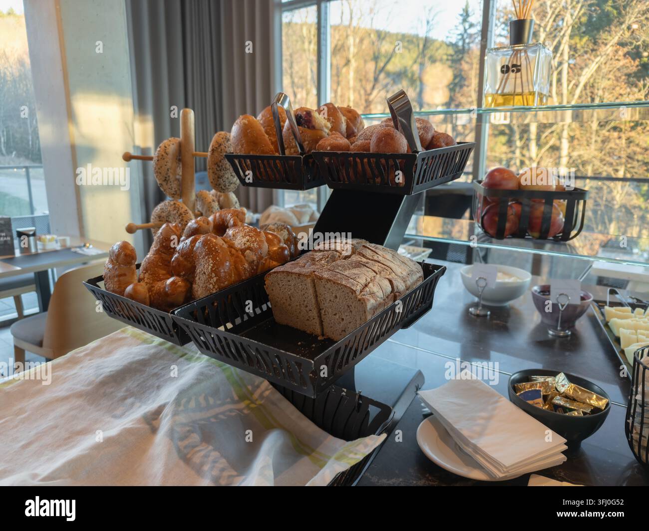 Pain artisanal et croissants dorés servis sur un présentoir moderne à plusieurs niveaux dans un restaurant lumineux, représentant un petit-déjeuner gourmet sain Banque D'Images