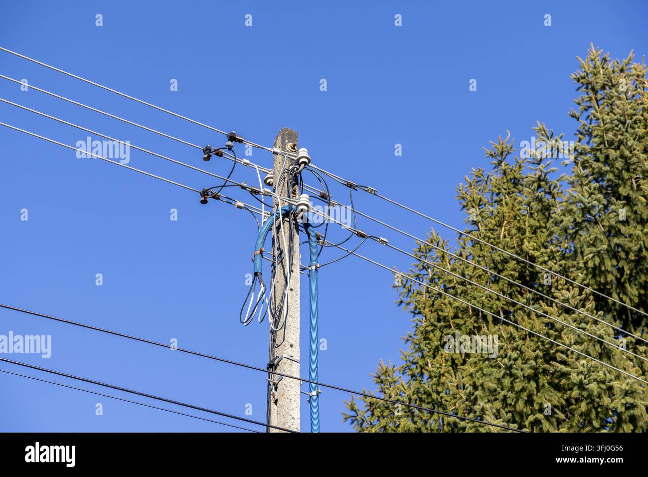 Un poteau électrique présente des lignes aériennes et des tubes de protection, représentant la connectivité moderne du réseau énergétique, la maintenance des services publics et l'industrie Banque D'Images