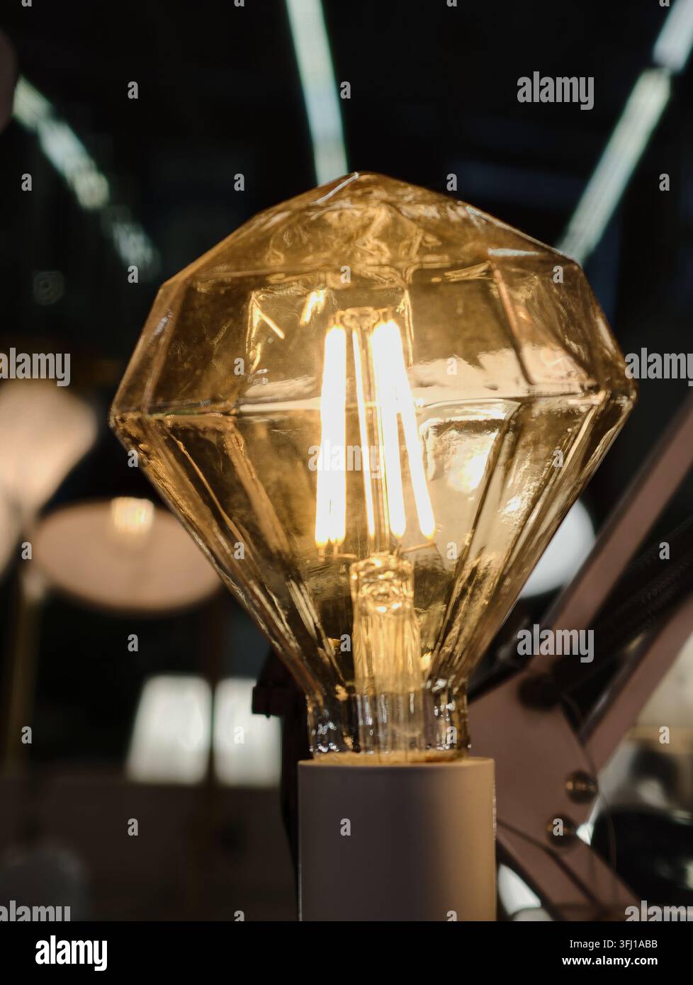 Ampoule LED décorative en forme de diamant à facettes avec un enveloppe en verre ambré. Filaments LED verticaux de style vintage ; culot E27. Banque D'Images