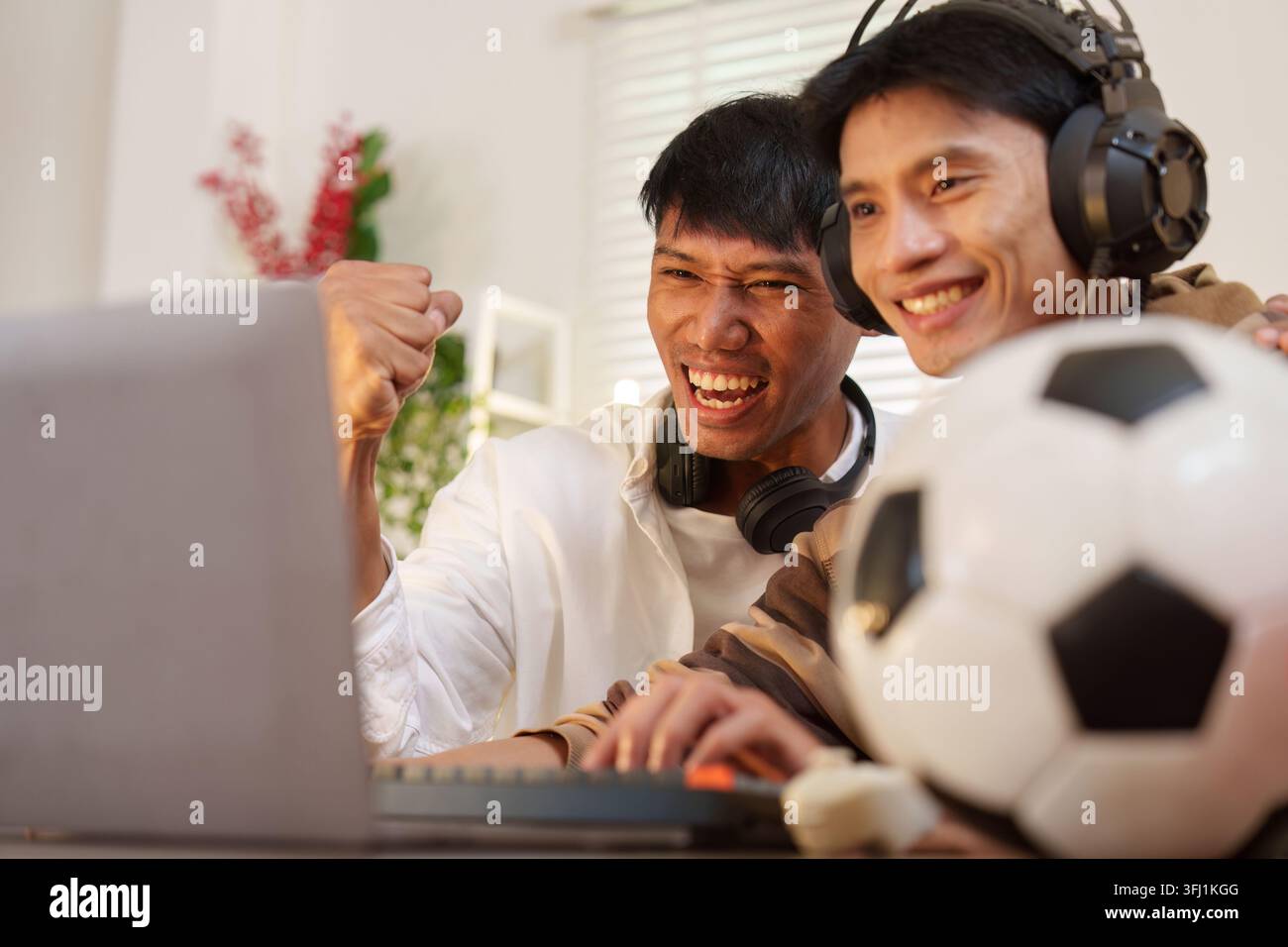 Hommes asiatiques regardant le match de football sur ordinateur portable à la maison Banque D'Images