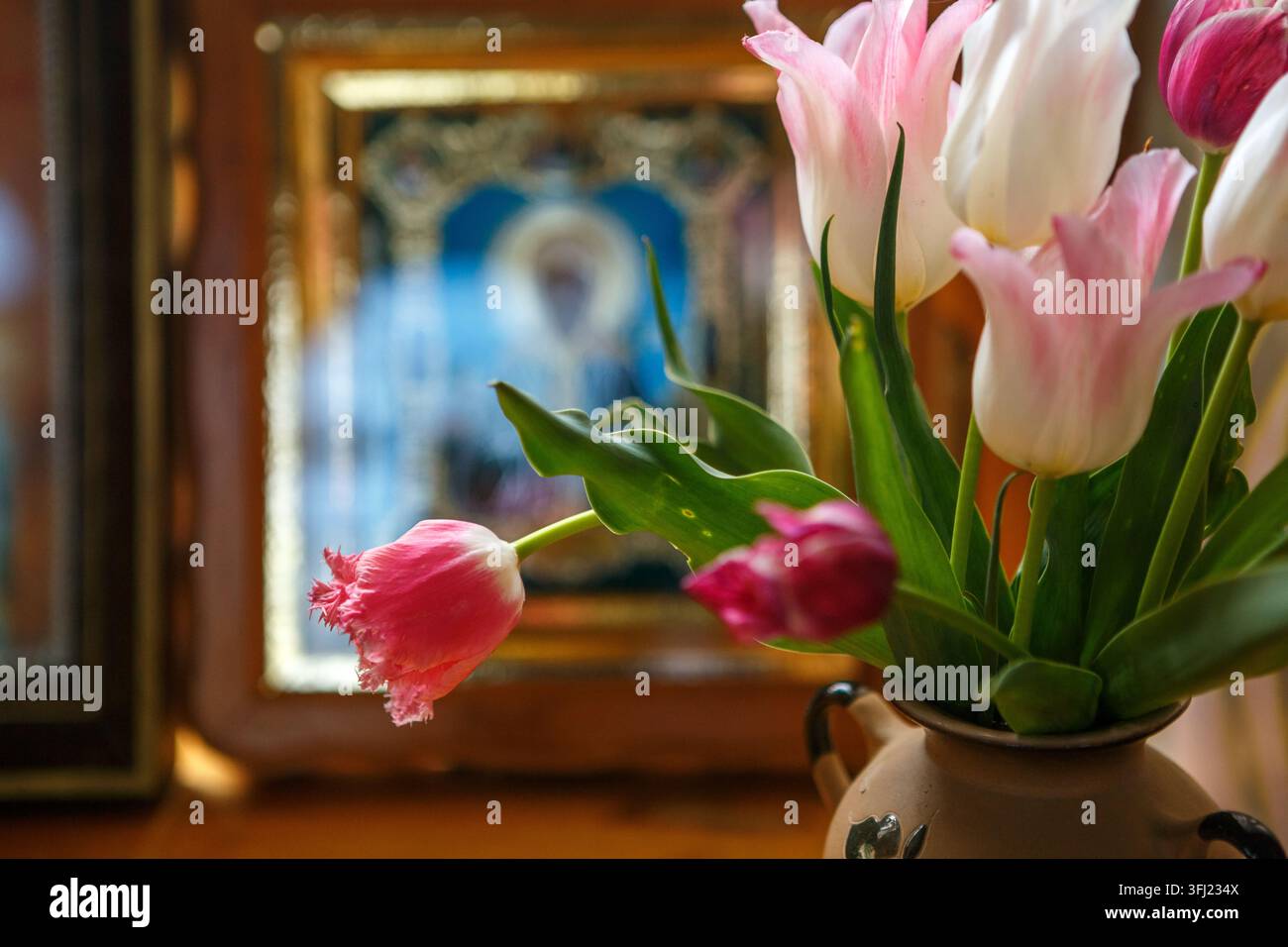 Tulipes roses et blanches dans un vase à côté d'une icône orthodoxe Banque D'Images