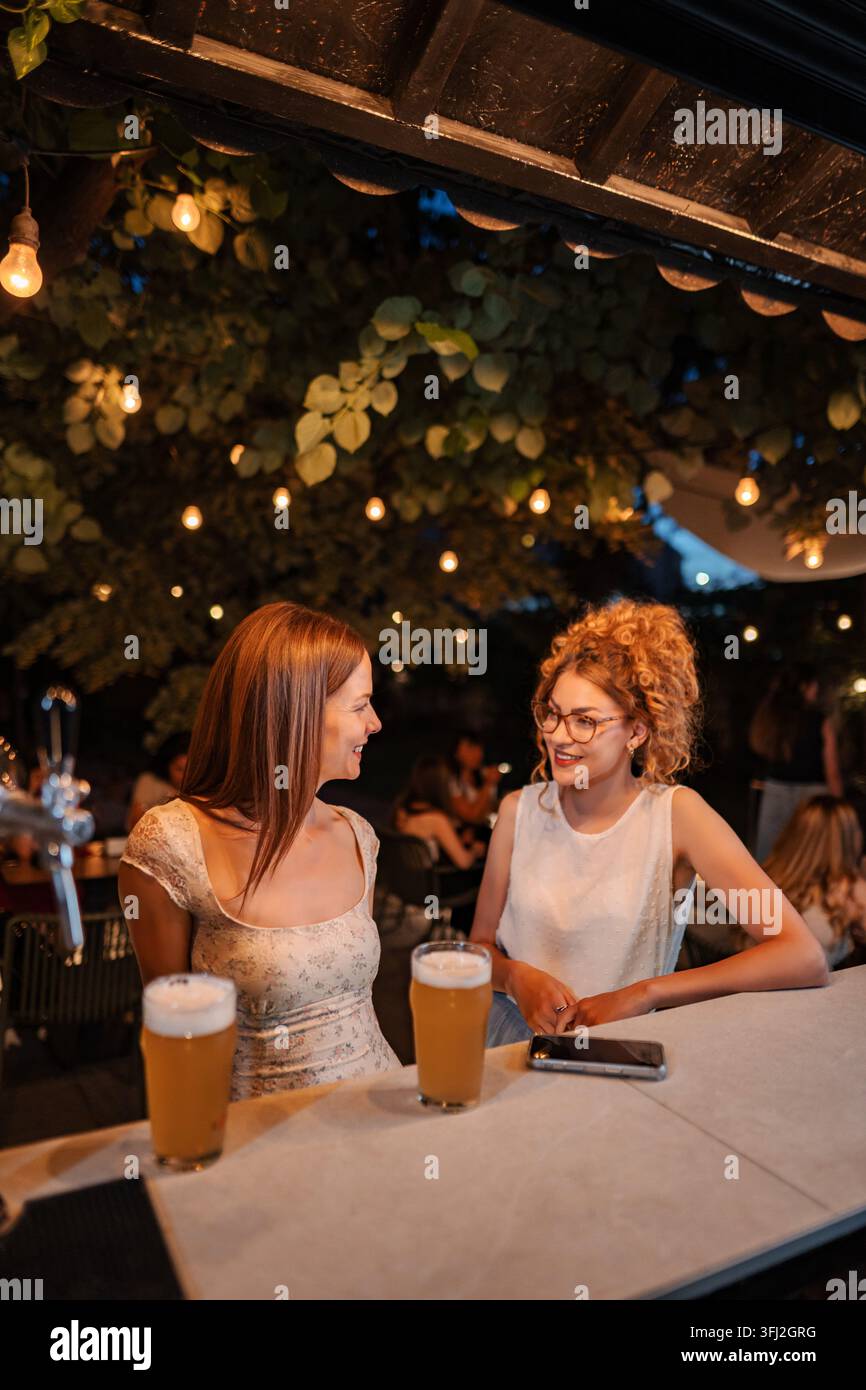 Des femmes profitant d'une bière dans un bar extérieur de nuit Banque D'Images