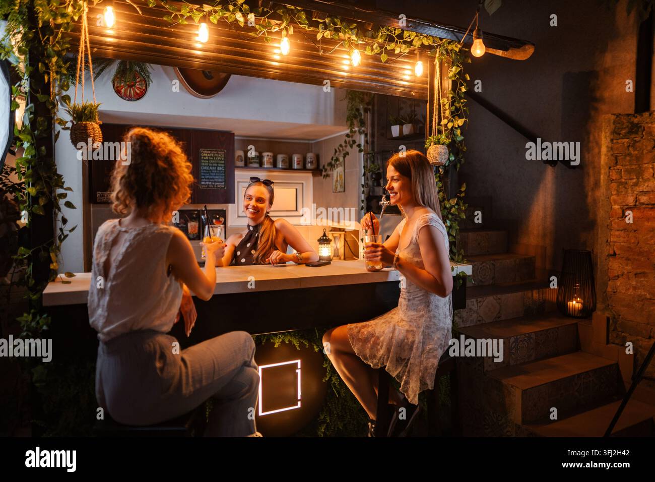 Trois jeunes amies adultes s'amusant et parlant au bar la nuit Banque D'Images