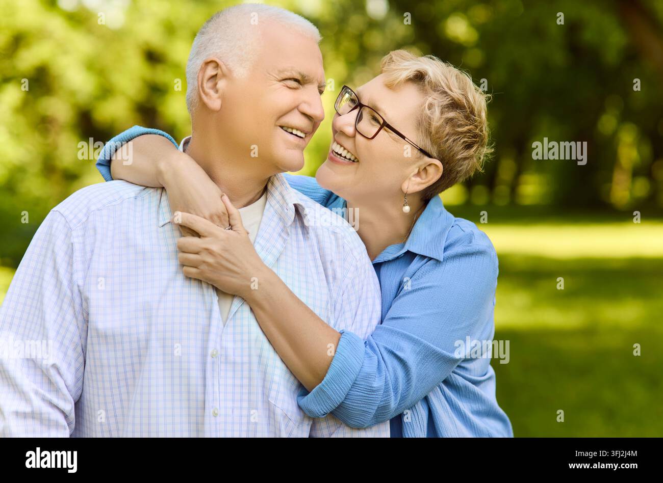 Couple de personnes âgées heureuses s'embrassant dans un parc ensoleillé, souriant avec amour et joie en plein air Banque D'Images