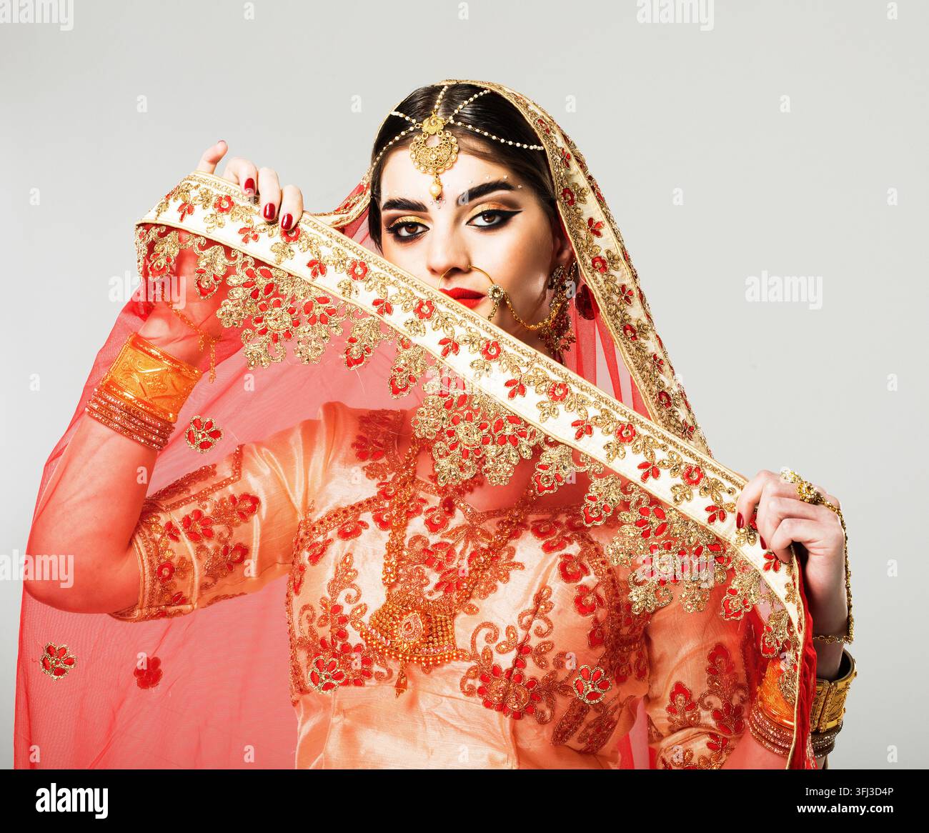 Jeune modèle hindoue avec des bijoux traditionnels. Costume indien en saree rouge. Une femme indienne ou musulmane couvre son visage. Banque D'Images
