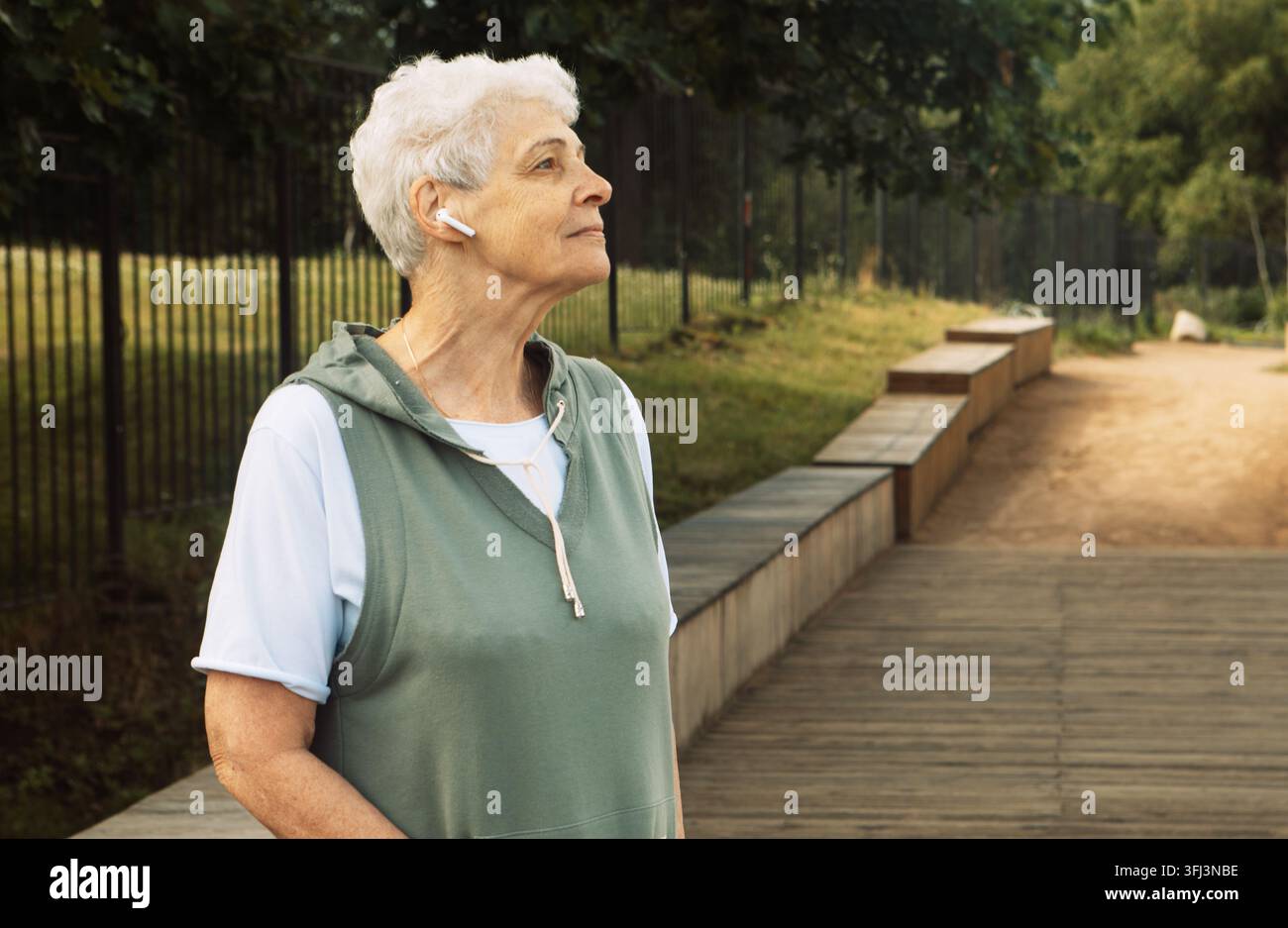Une femme âgée aux cheveux courts et bouclés marche dans un parc en été. Banque D'Images