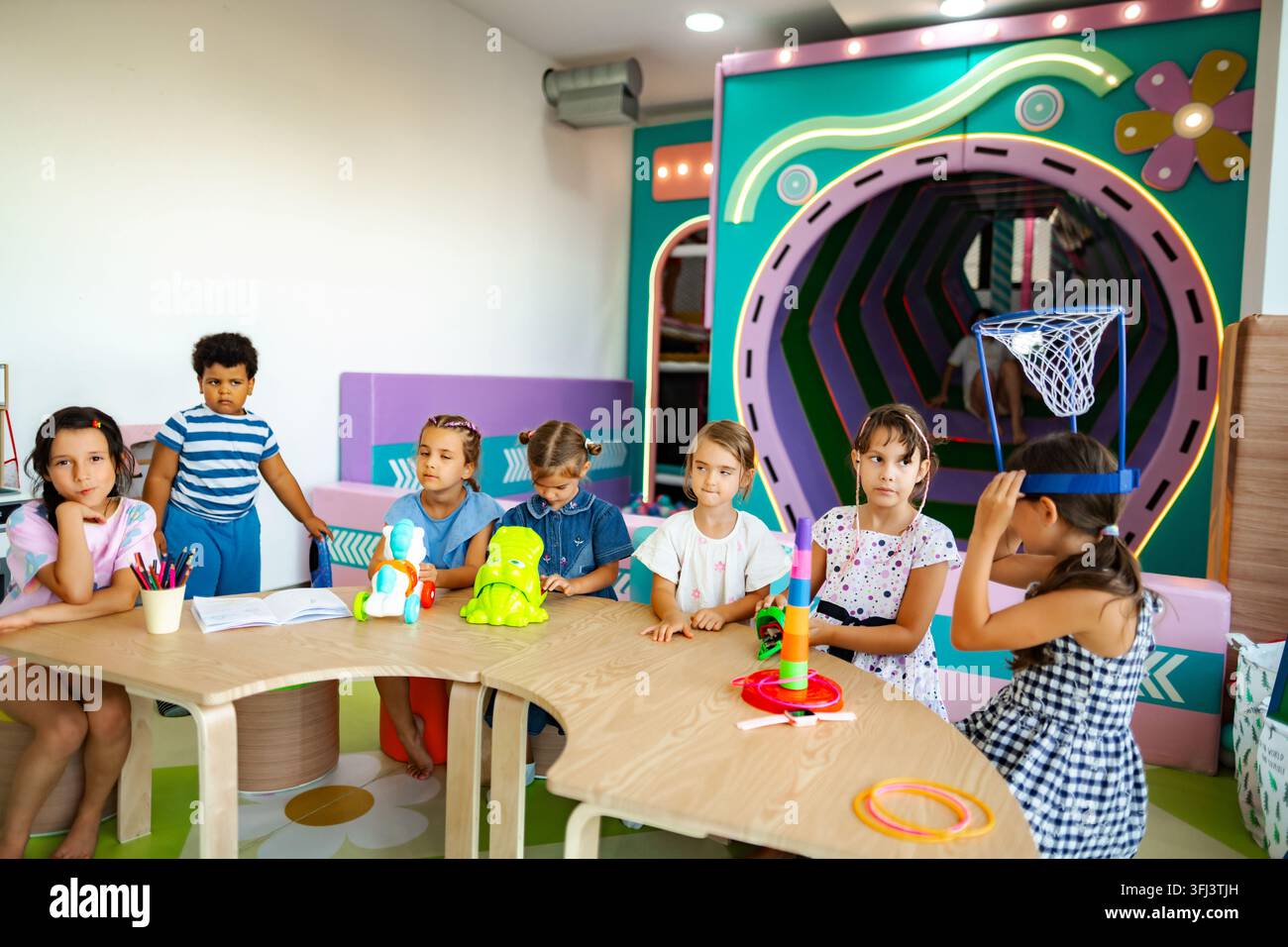 Enfants jouant avec des jouets et dessinant dans une salle de jeux colorée de la maternelle Banque D'Images