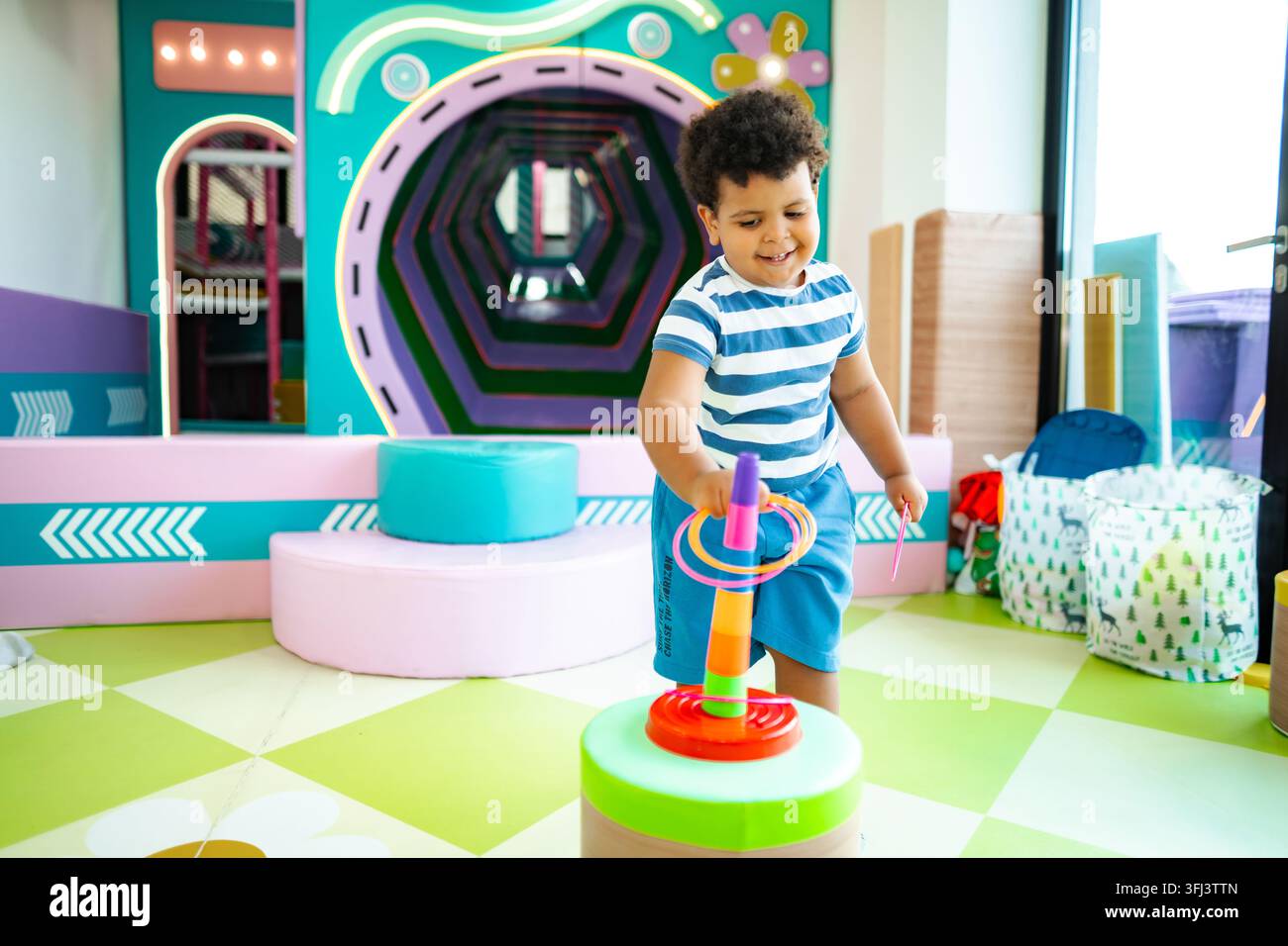 Enfant souriant jouant au lancer de anneaux dans une zone de jeux douce et colorée Banque D'Images