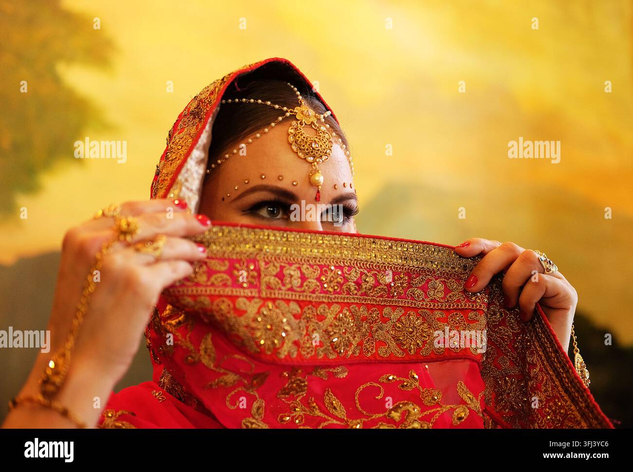 Jeune modèle hindoue avec des bijoux traditionnels. Costume indien en saree rouge. Une femme indienne ou musulmane couvre son visage. Banque D'Images