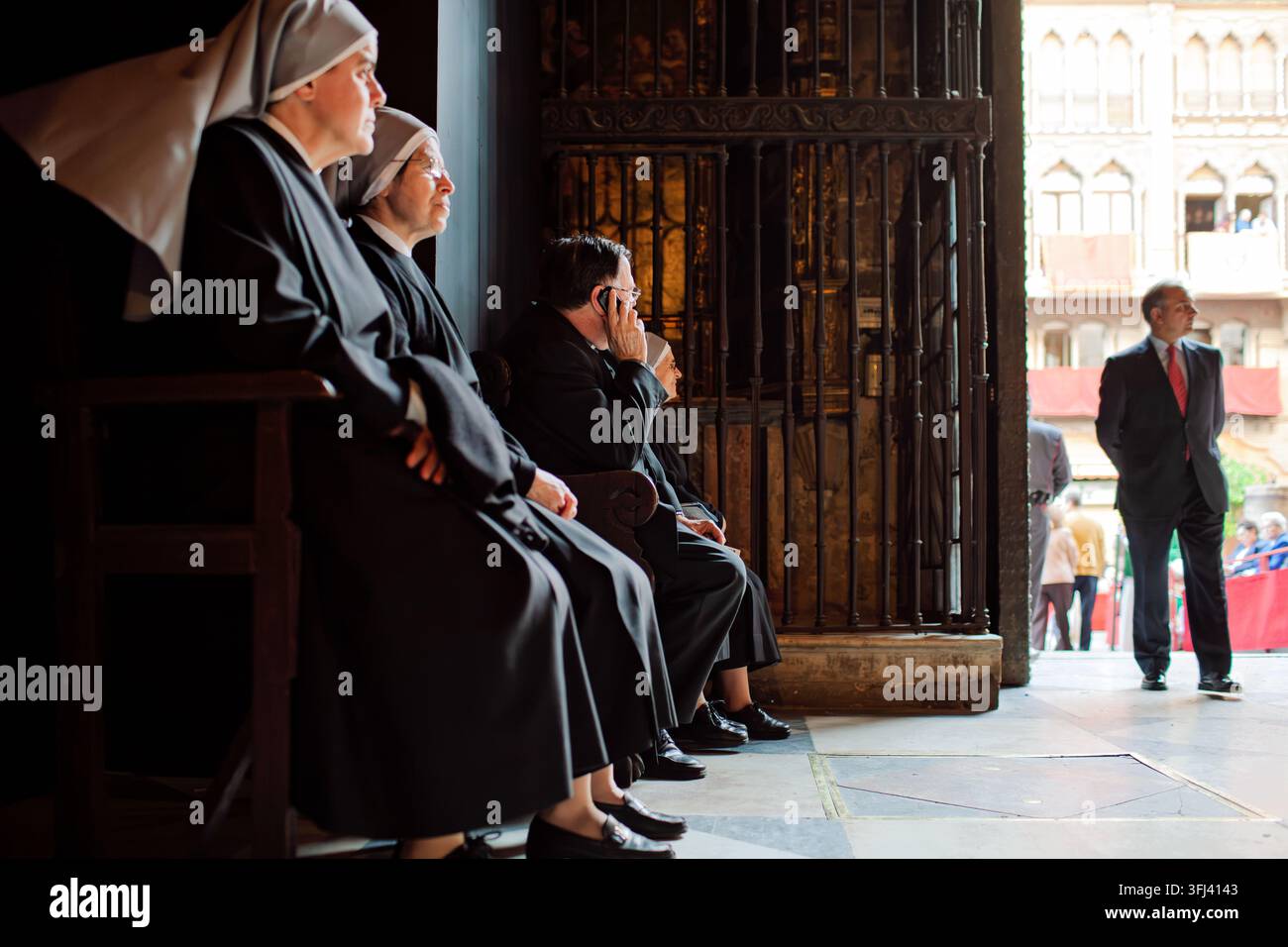 Des religieuses et un prêtre sont assis à l'intérieur de la cathédrale de Séville, observant attentivement l'extérieur en attendant le début des processions de la Semaine sainte en Andalousie Banque D'Images