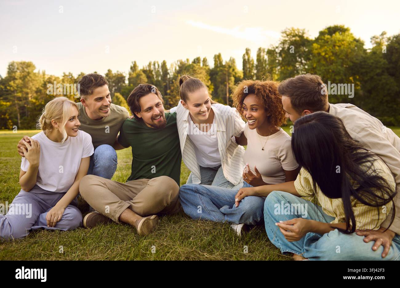 Amis divers et heureux discutant et riant assis ensemble sur l'herbe dans le parc Banque D'Images