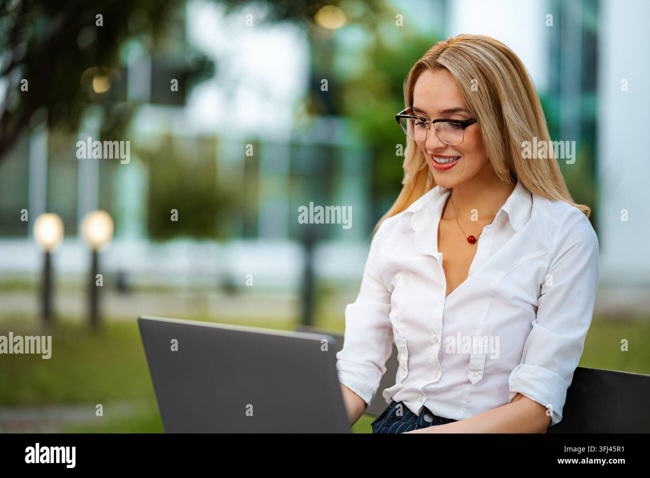 Femme blonde travaillant sur un ordinateur portable dans un cadre de parc Banque D'Images