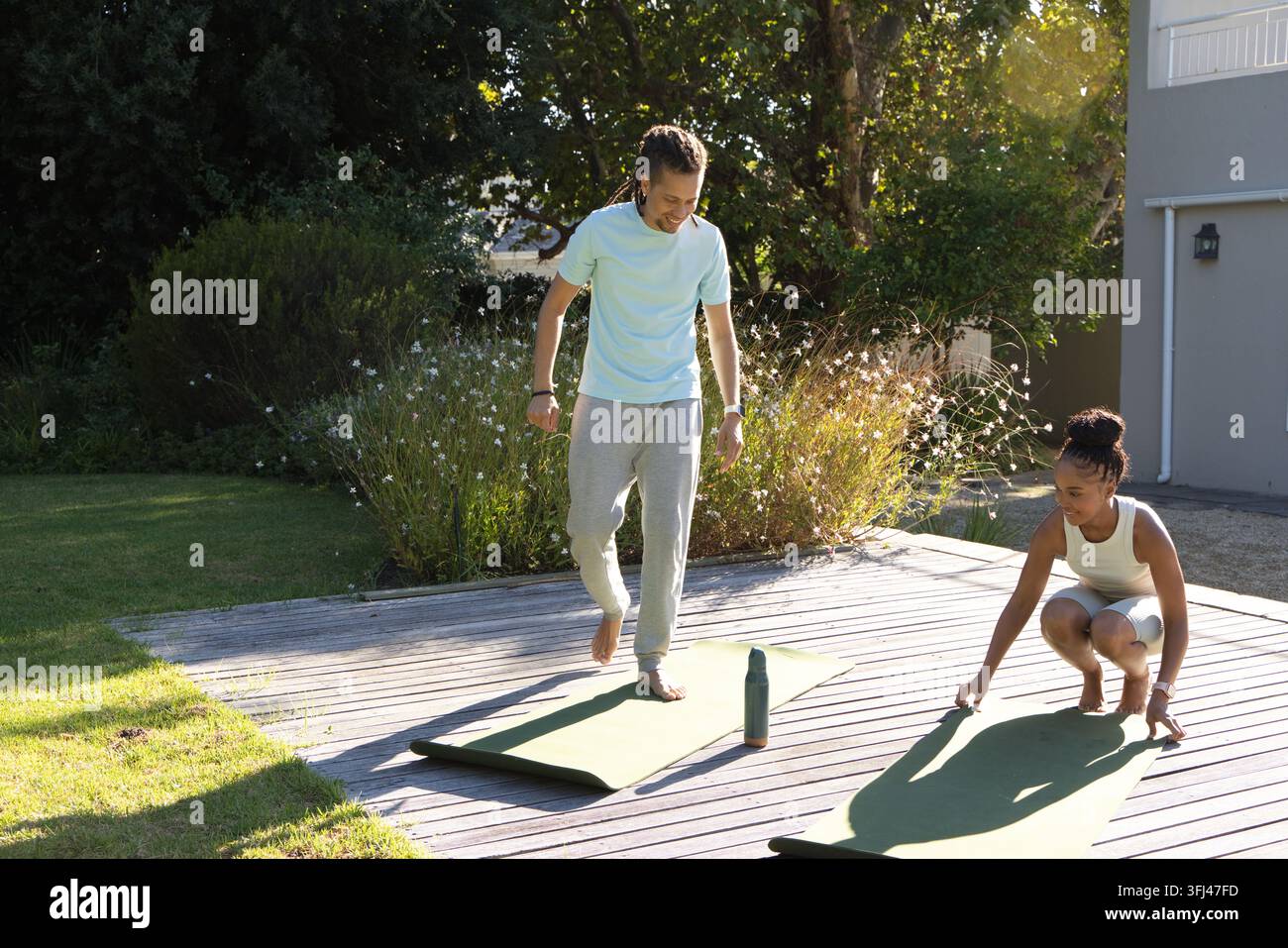 Couple afro-américain en tee et short préparant sur une terrasse en bois en posant des tapis verts et une bouteille. Arrière-cour, extérieur, fitness, yo Banque D'Images