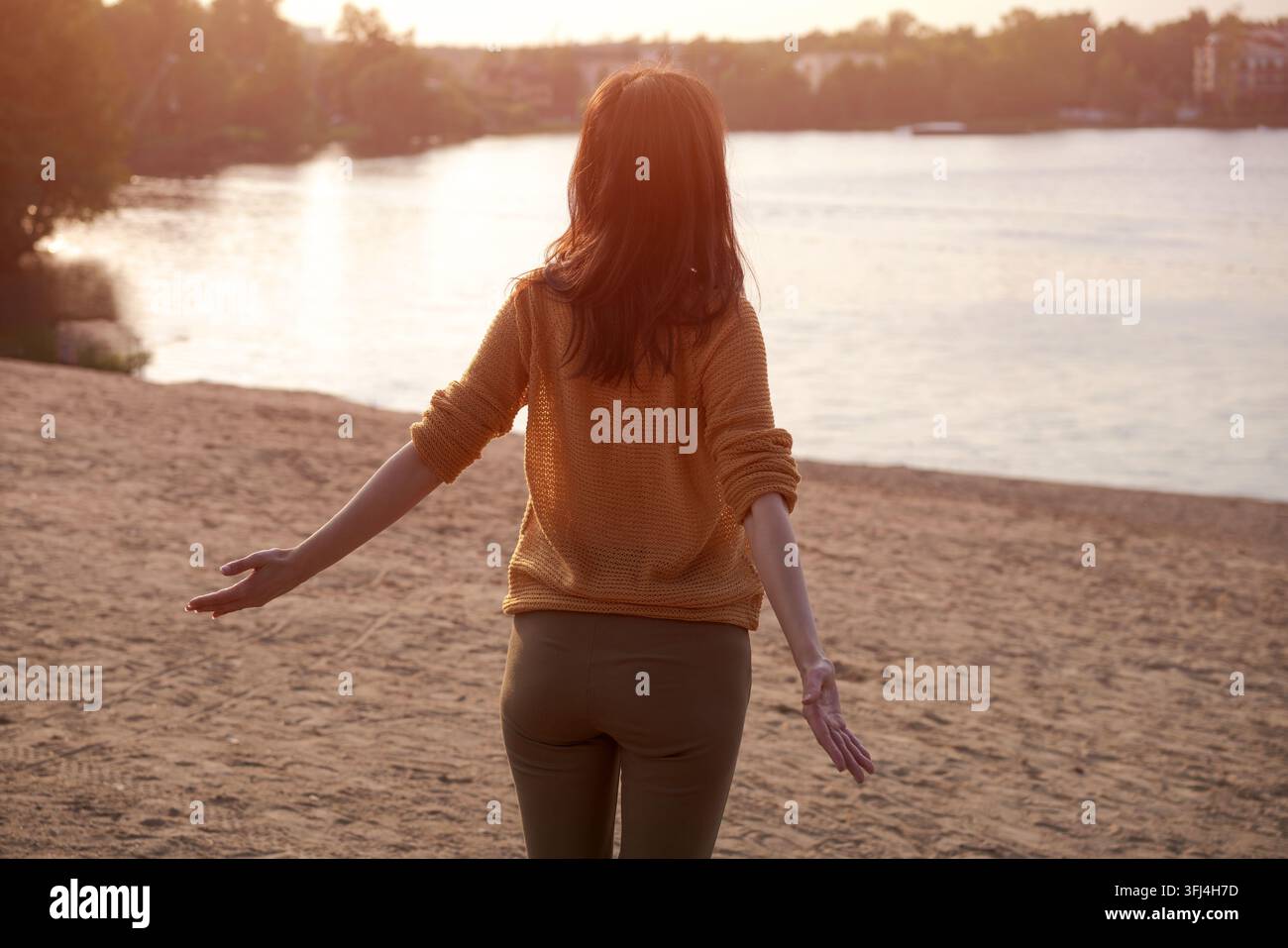 Dos d'une femme aux bras ouverts sur une plage de sable au coucher du soleil Banque D'Images