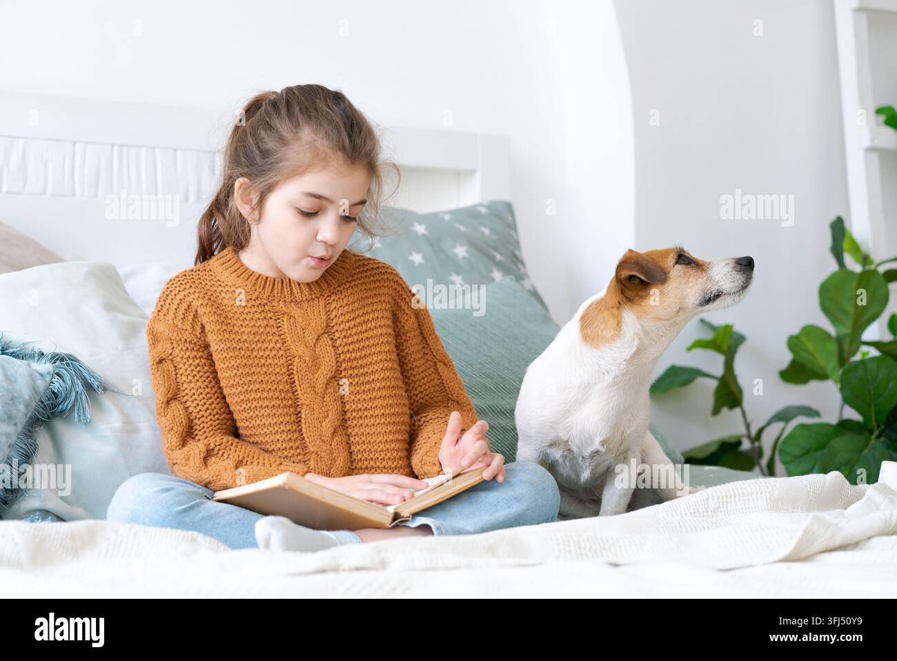 Enfant caucasien avec un livre d'histoires et son terrier près d'une plante Banque D'Images