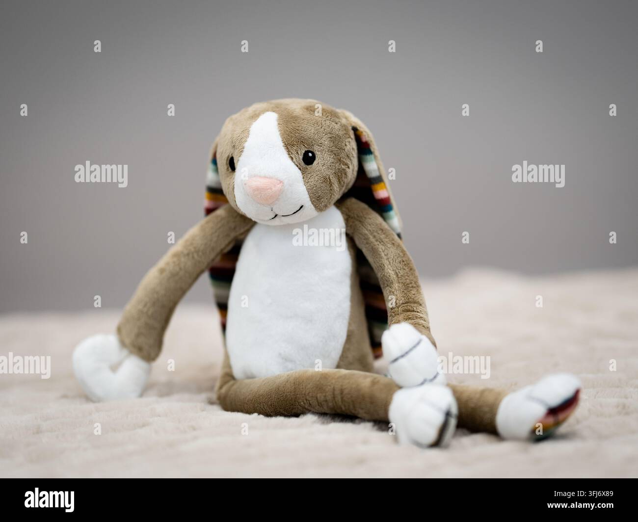 Jouet lapin en peluche douce posé sur une couverture légère contre un fond neutre avec une profondeur de champ peu profonde. Banque D'Images