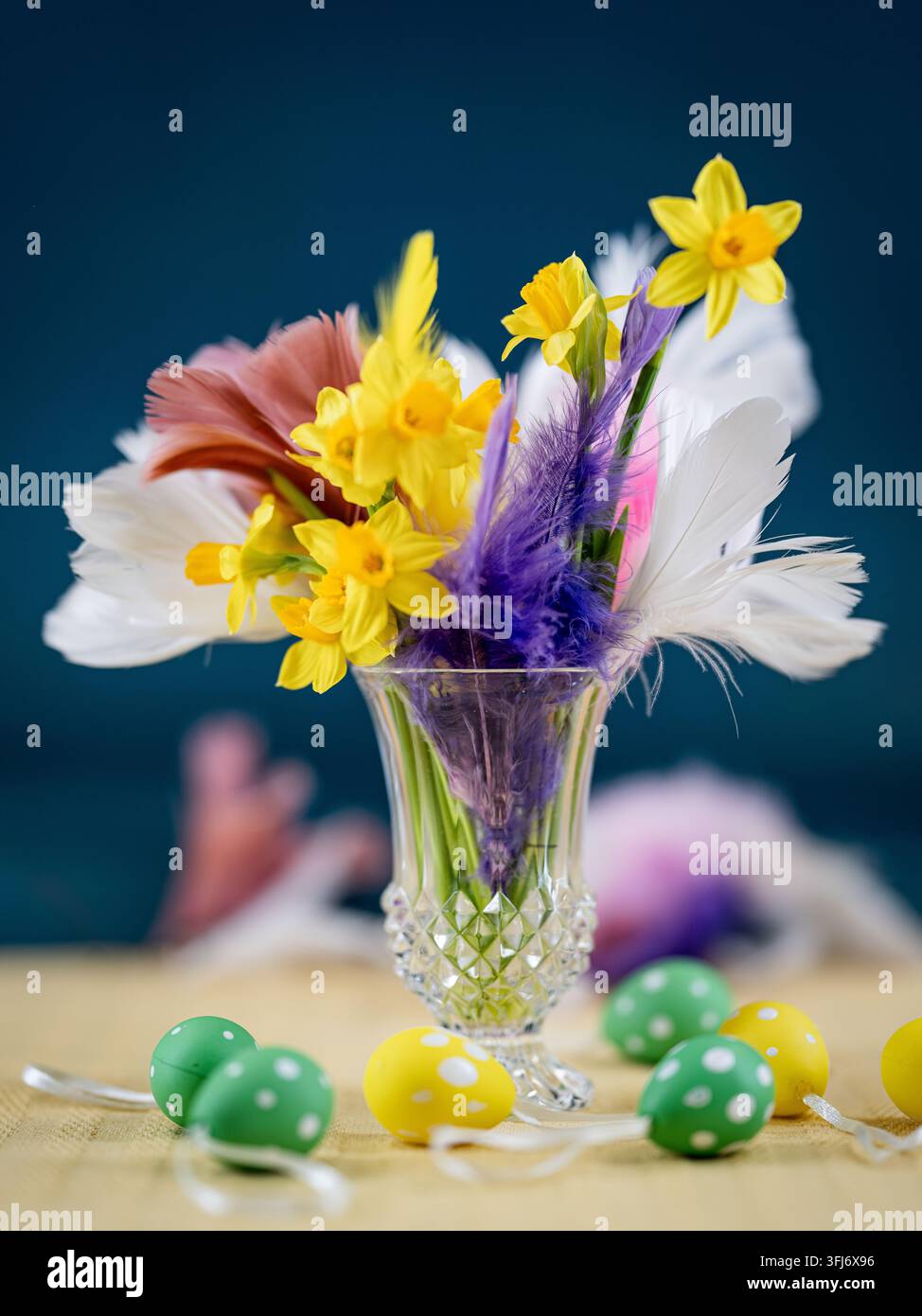 Arrangement printanier de jonquilles jaunes et de plumes colorées dans un vase en verre avec des œufs de Pâques décoratifs. Banque D'Images