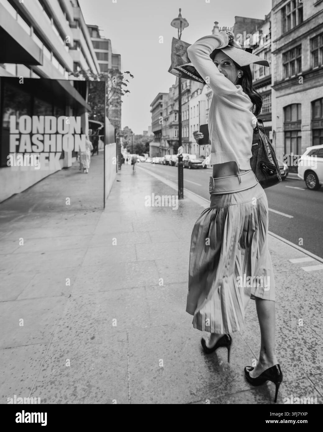 Une dame élégante protège ses cheveux de la pluie alors qu'elle se rend à un défilé de mode pendant la London Fashion Week. Banque D'Images