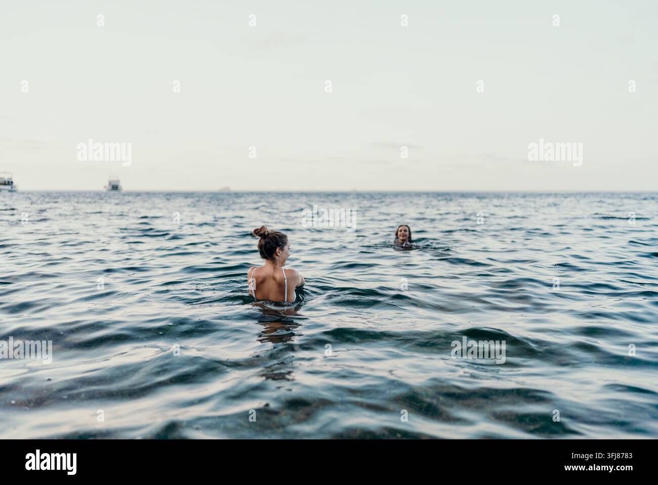 Femmes nageant dans l'océan. Deux femmes profitant d'une baignade relaxante en vacances d'été dans l'océan avec des bateaux au loin. Banque D'Images