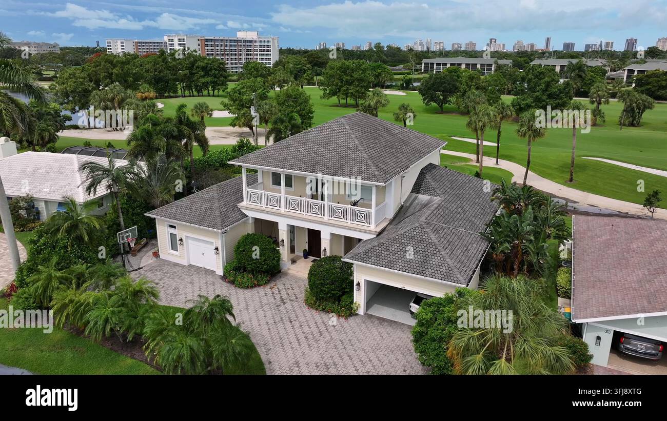 Maison élégante à deux étages en Floride près d'un terrain de golf. Des palmiers luxuriants et des pelouses bien entretenues entourent la propriété. Les immeubles de grande hauteur au loin ajoutent à le Banque D'Images