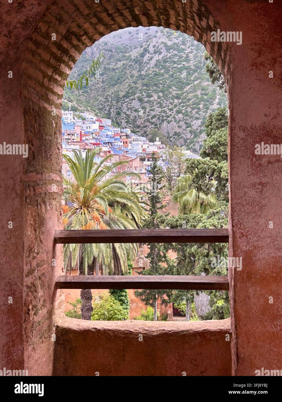 Vue de la ville de colline de Chefchaouen encadrée par une arche de briques traditionnelle et une végétation luxuriante dans le nord du Maroc. Banque D'Images