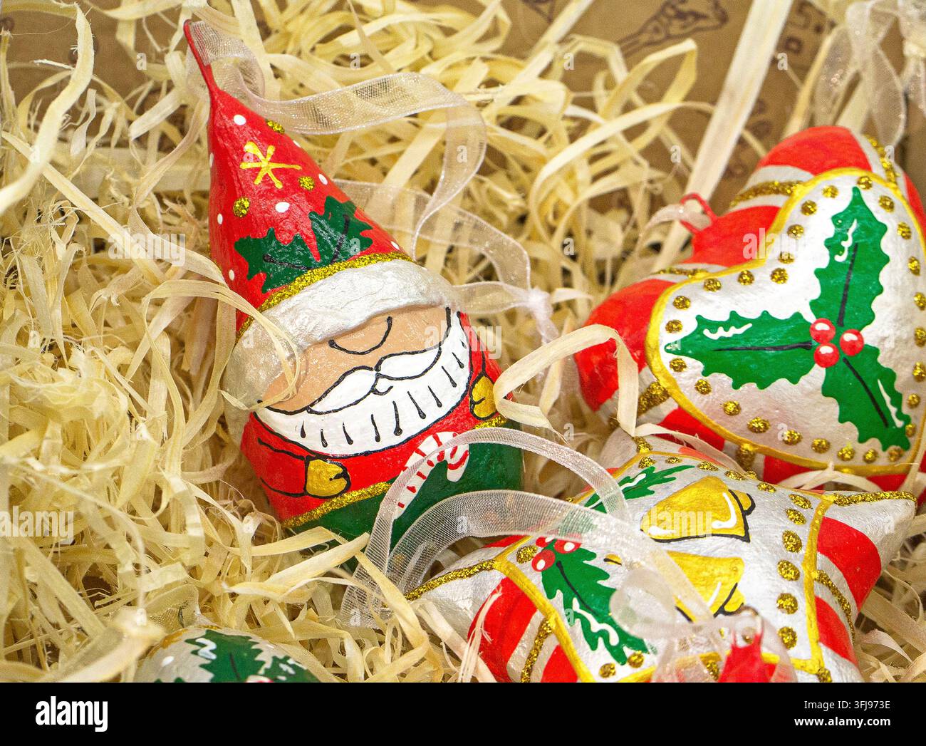 Vue rapprochée de décorations de Noël colorées peintes à la main, comprenant une figurine du Père Noël et des ornements en forme d'étoile reposant dans un emballage en paille déchiré Banque D'Images