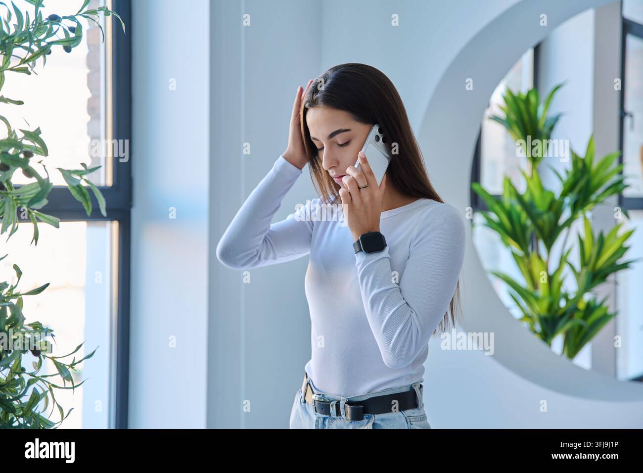 Jeune femme stressée tenant sa tête tout en parlant au téléphone à l'intérieur Banque D'Images