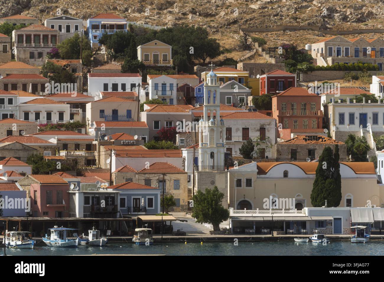 Une vue depuis une colline sur Halki montre des maisons lumineuses avec des toits rouges et des murs pastel doux s'élevant au-dessus de l'eau calme, avec l'église d'Agios Nikolaos située parmi les c Banque D'Images