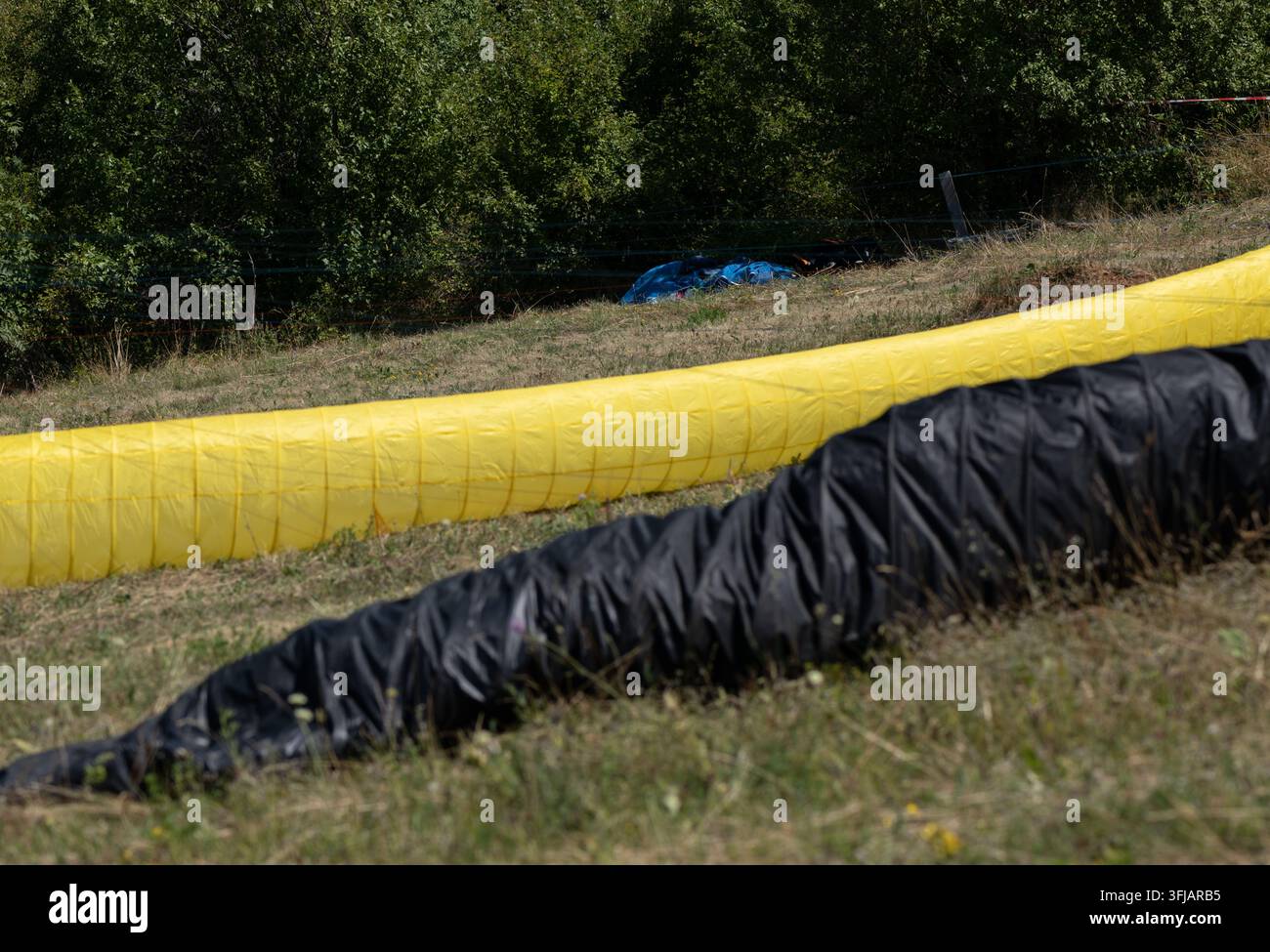 Bâches de parapente jaunes et noires sur l'herbe. Forêt verte en arrière-plan, capturant la beauté, la liberté et l'excitation de l'aventure en plein air. Banque D'Images