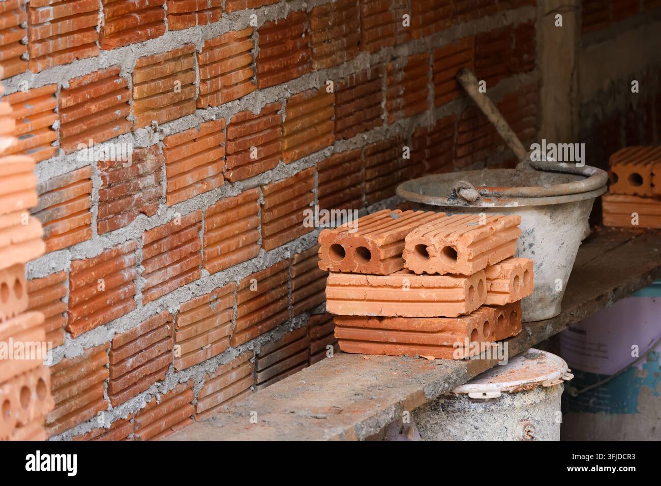 Un mur de briques inachevé et des briques creuses empilées à côté d'un seau de construction dans un espace de maçonnerie Banque D'Images