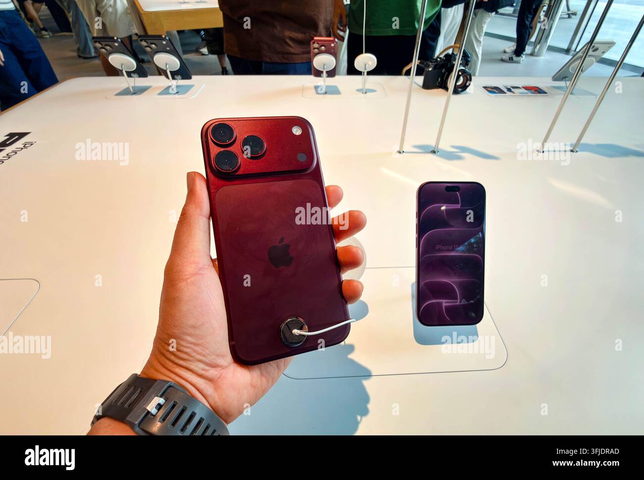 BANGKOK, THAÏLANDE - 19 SEPTEMBRE 2026 : Homme tenant un nouveau smartphone iPhone 18 Pro Max bordeaux dans la main au-dessus d'une table d'exposition à l'intérieur de l'Apple Store Centra Banque D'Images