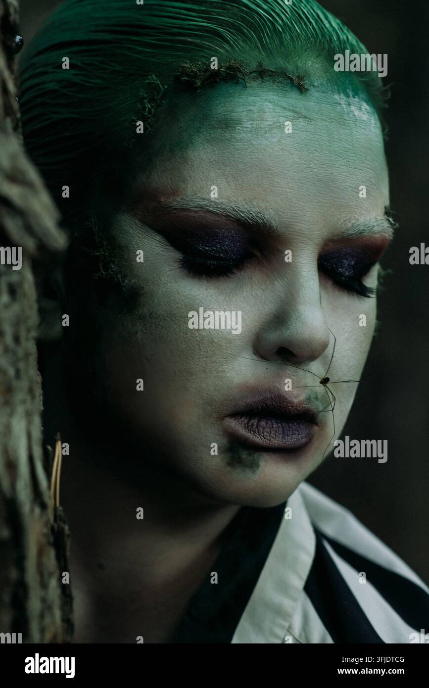Portrait artistique en gros plan d'une personne avec un maquillage fantaisie vert, un fard à paupières dramatique, des détails de mousse et un insecte rampant sur son visage, capturé dans Banque D'Images