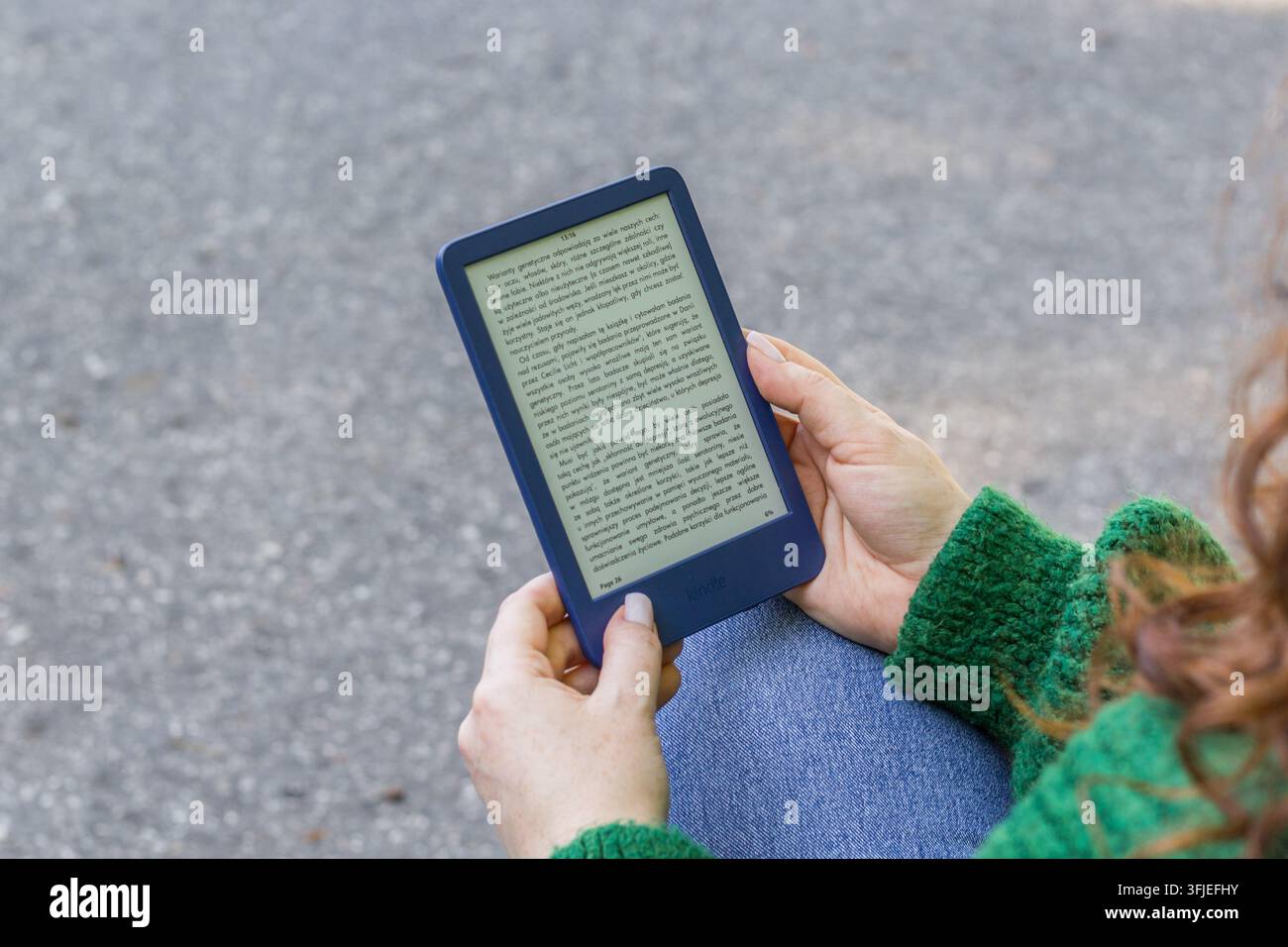 Personne lisant un livre électronique sur une liseuse électronique en plein air, tenant l'appareil à deux mains. Banque D'Images