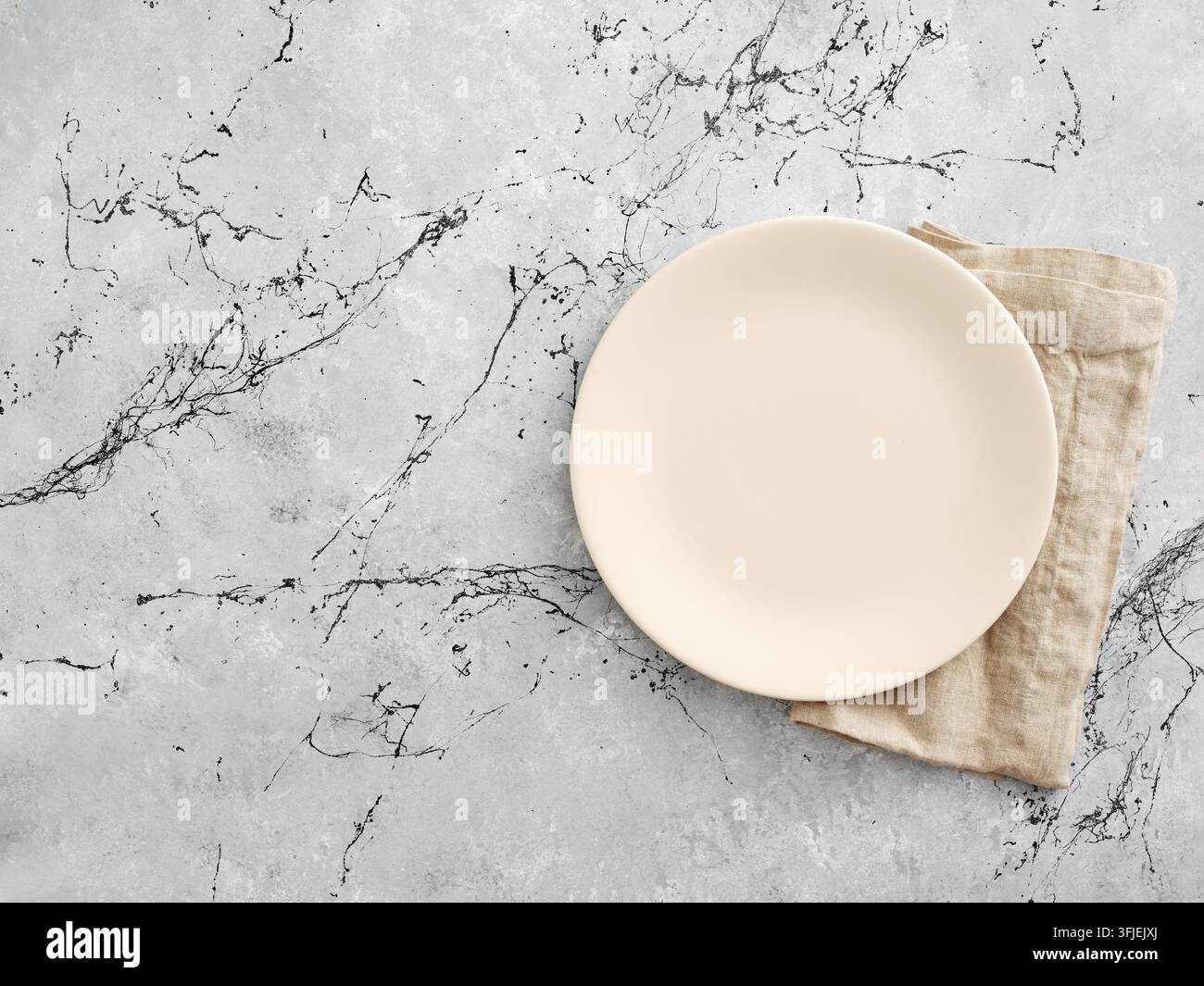 Assiette vide beige avec serviette en lin sur une table grise texturée, offrant un espace suffisant pour le design ou les menus Banque D'Images