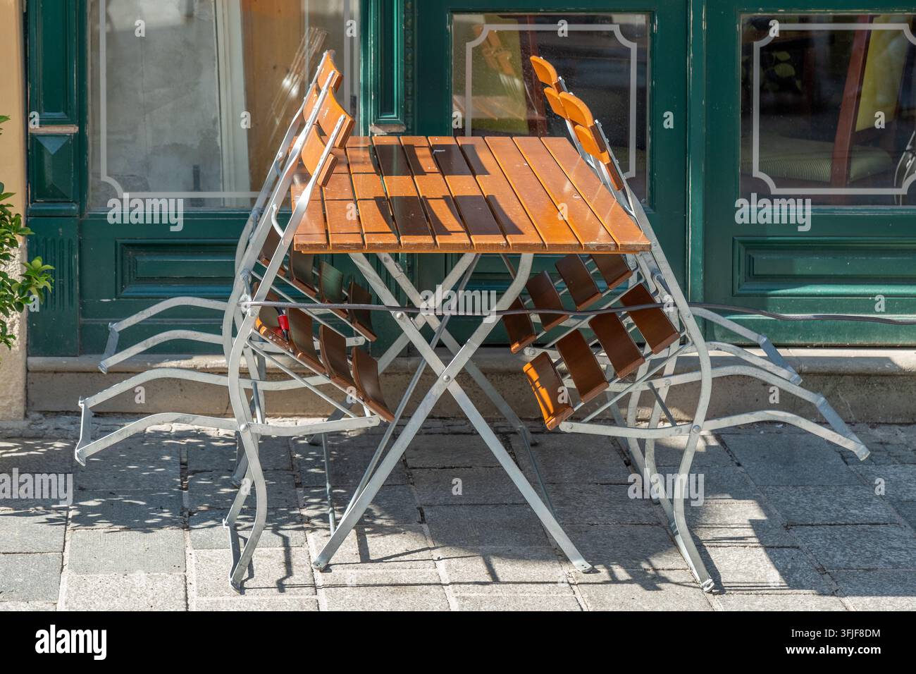Une table de café extérieure vide avec des chaises pliées se dresse devant une vitrine verte. Banque D'Images