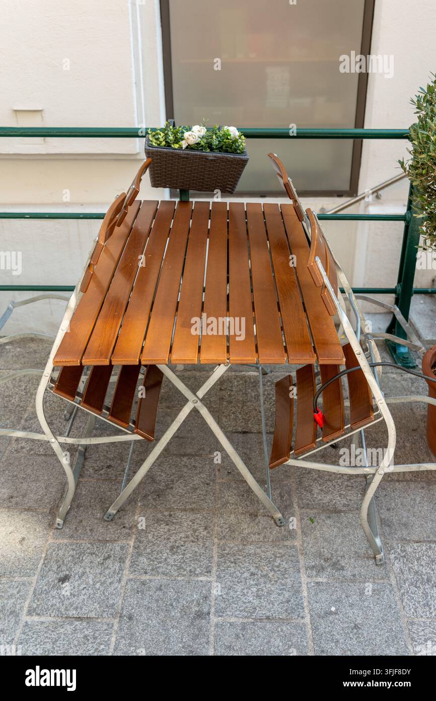 Une table de café extérieure vide avec des chaises en bois et un bac à fleurs se trouve sur une terrasse en pierre. Banque D'Images