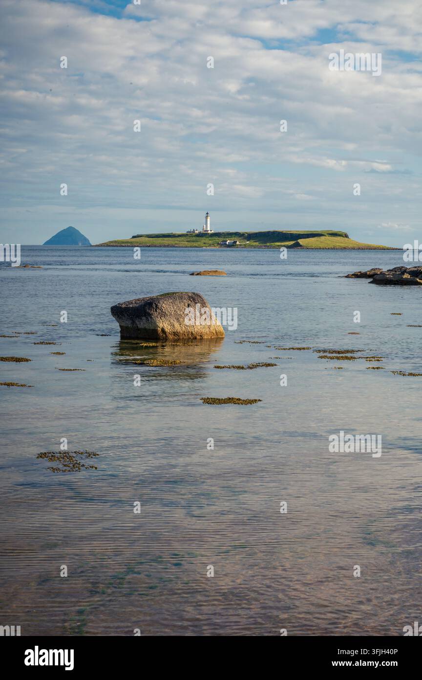 Phare de Pladda vu au loin derrière un gros rocher dans les eaux de la plage de Kildonan, île d'Arran, Écosse (format vertical) Banque D'Images