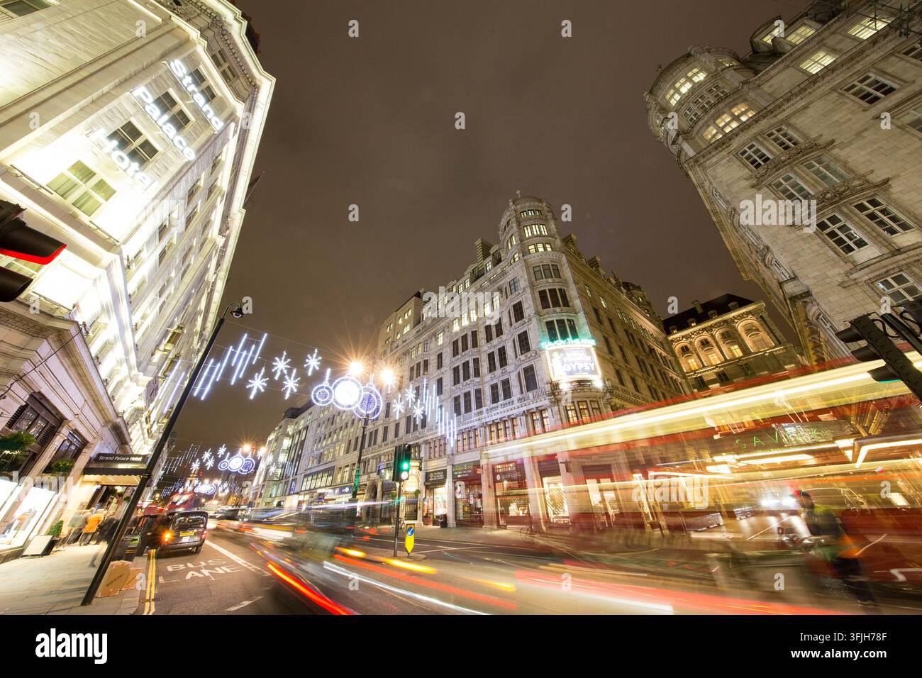 Des véhicules filent devant le Strand Palace Hotel et le Savoy Theatre du Strand à Londres, illuminés par des lumières festives de Noël. Banque D'Images