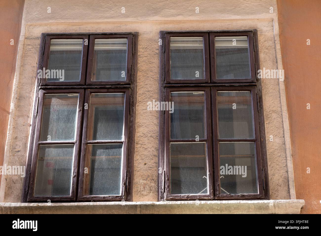 Deux vieilles fenêtres en bois sont encastrées dans une façade en stuc érodée sous une lumière chaude du jour. Banque D'Images