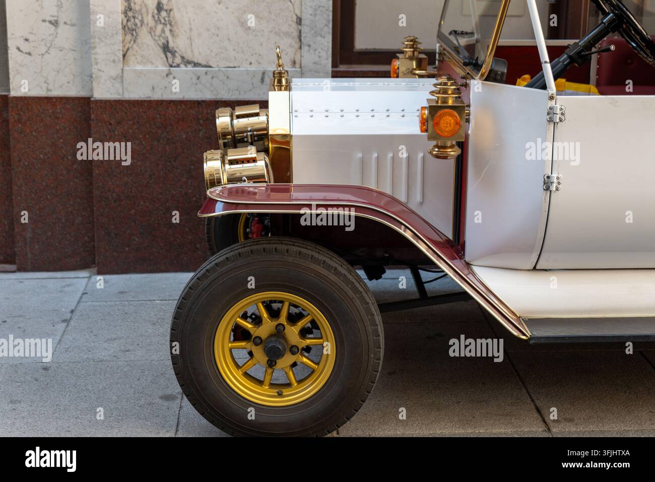 Une voiture vintage montre une roue avant, des phares en laiton et un pare-chocs marron à côté d'un mur de pierre. Banque D'Images