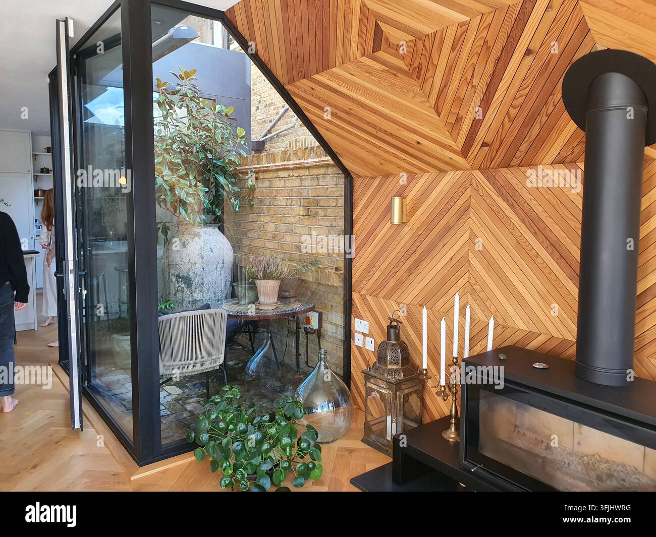 Un espace intérieur contemporain mettant en vedette un mur et un plafond lambrés en épingle à cheveux saisissants, avec un poêle à bois noir et un conduit d'évacuation exposé. Banque D'Images