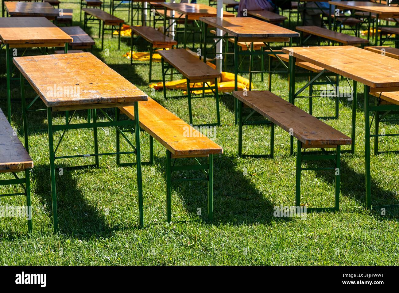 Des rangées de bancs et de tables en bois vides sont posées sur un terrain herbeux en plein air. Banque D'Images