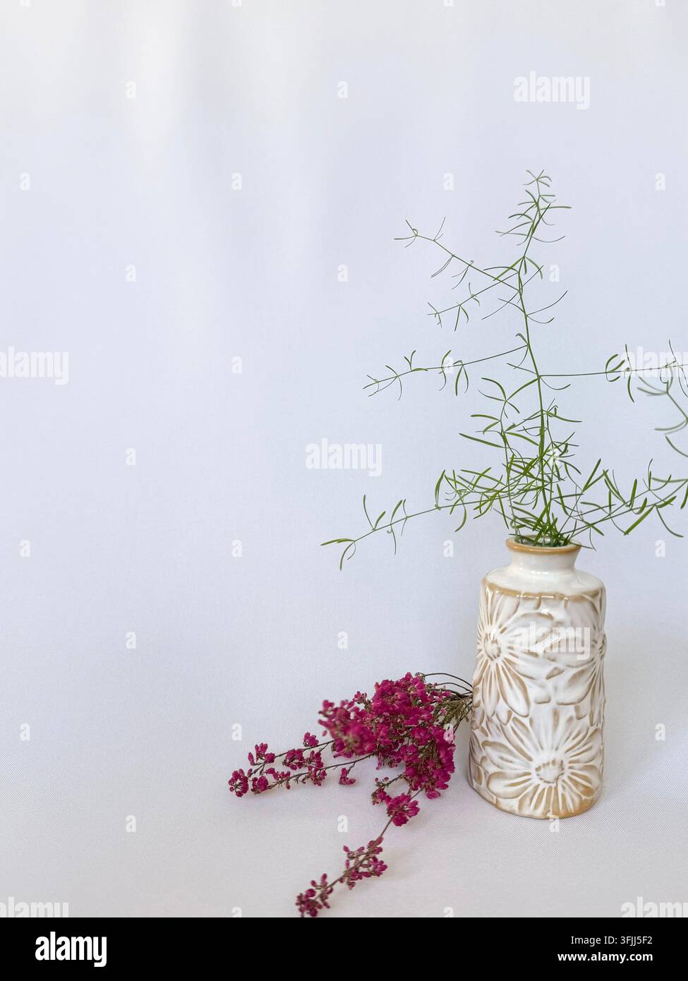 Nature morte florale minimaliste avec des fleurs roses et du feuillage vert dans un vase en céramique décoratif sur fond clair avec espace de copie Banque D'Images