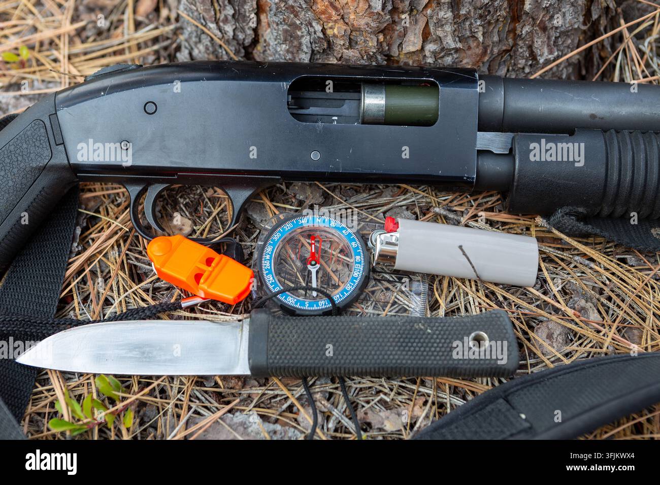 Kit de survie avec fusil à pompe noir, compas magnétique, couteau à lame fixe et briquet sur le fond de la forêt Banque D'Images