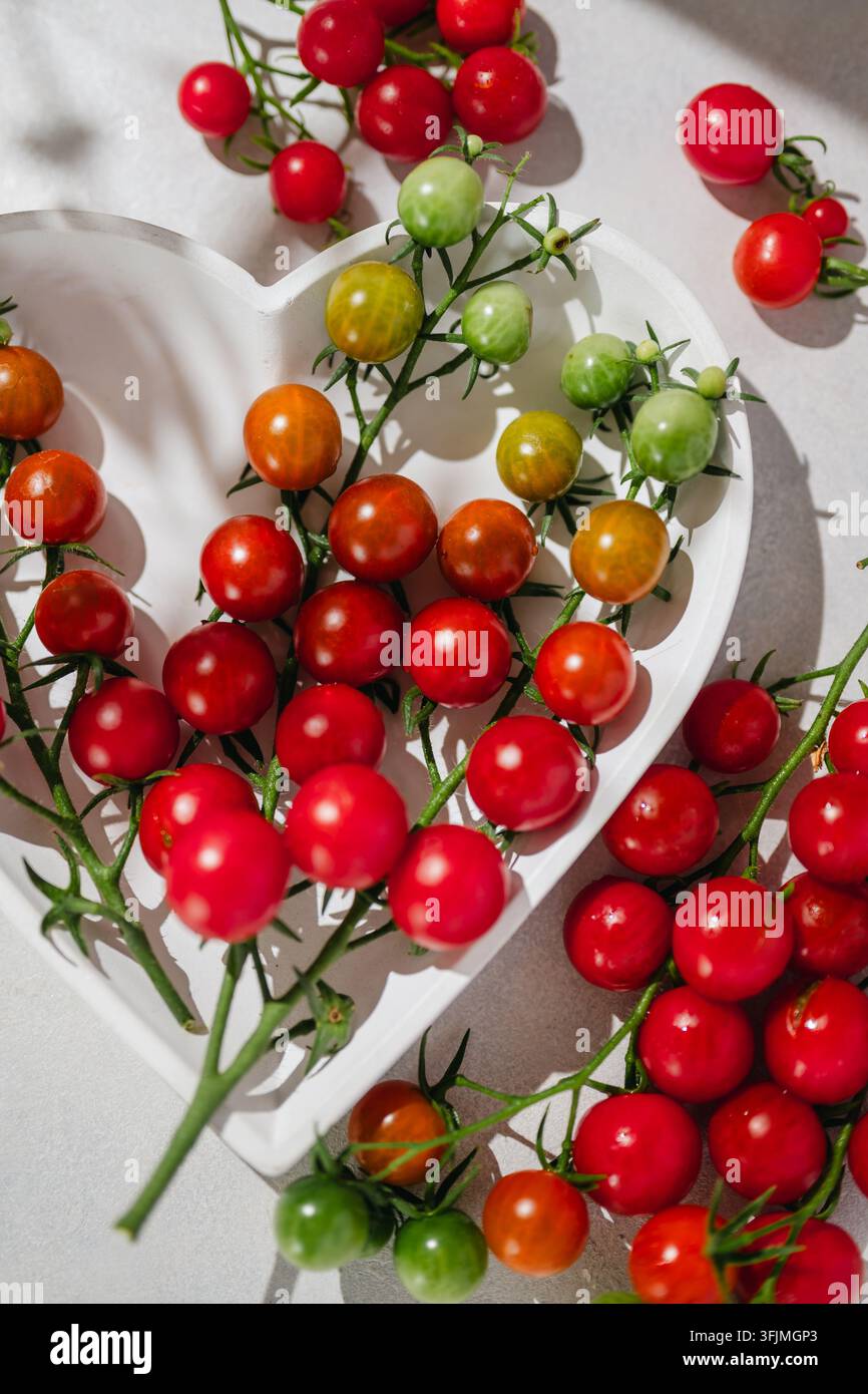Tomates cerises colorées sur des vignes dans un plat en forme de cœur blanc Banque D'Images