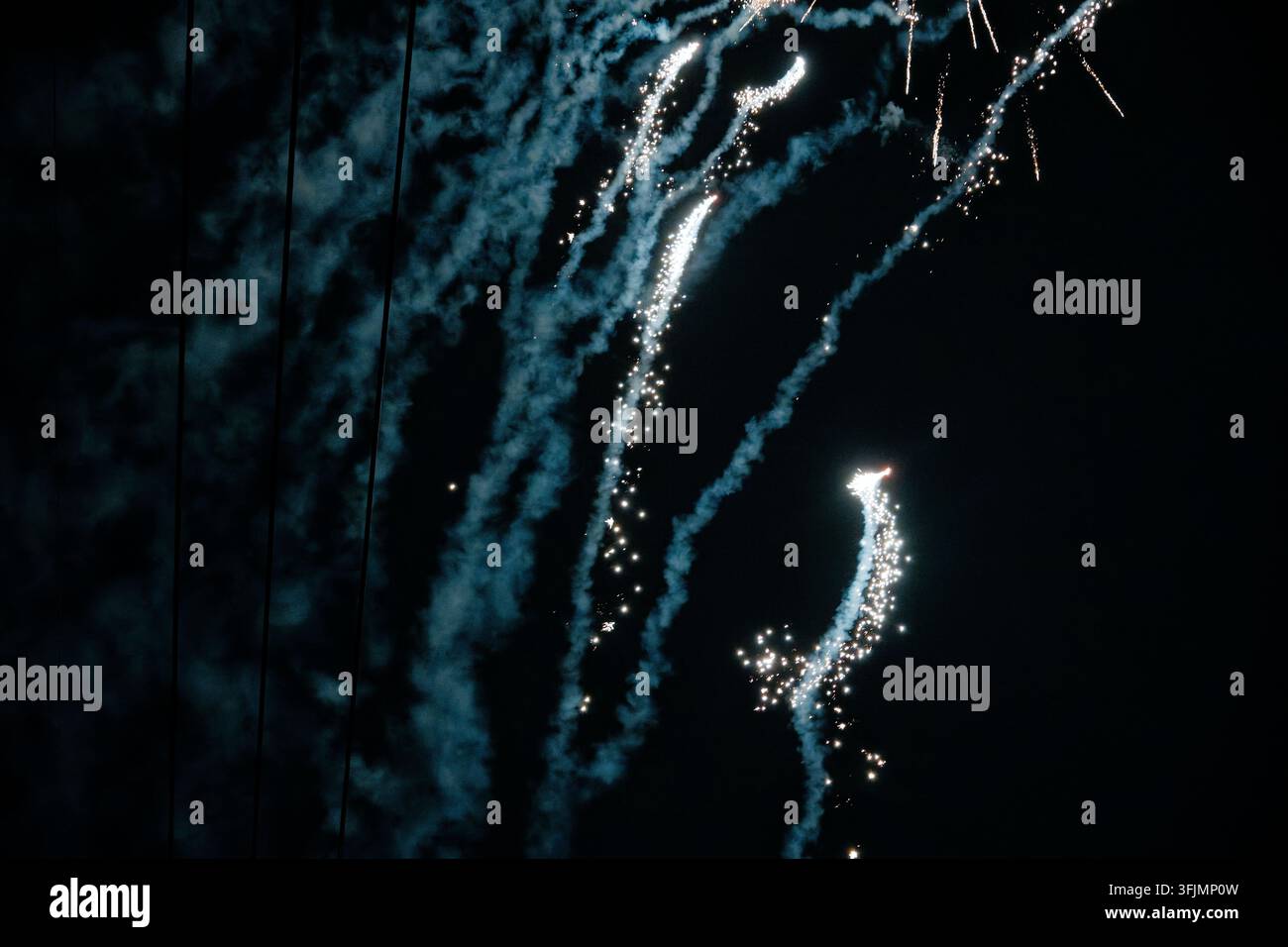 Les fusées de feux d'artifice s'élèvent en laissant des traînées bleues étincelantes à travers la fumée dérivante, brillant intensément contre un ciel nocturne sombre. Banque D'Images