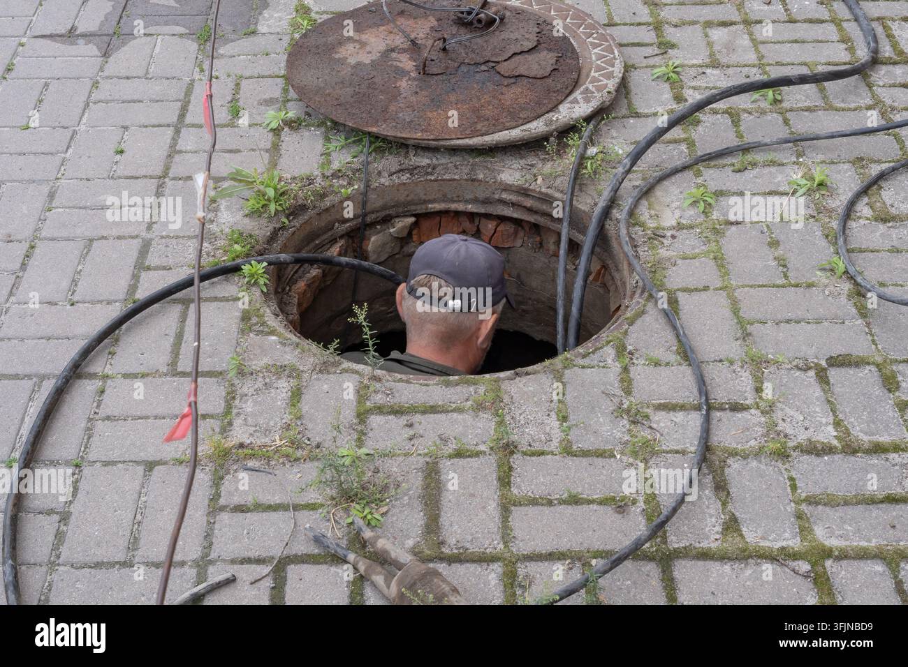 Les techniciens inspectent les lignes de communication souterraines à une bouche d'égout ouverte à côté de bâtiments urbains historiques et de drapeaux ukrainiens. Banque D'Images